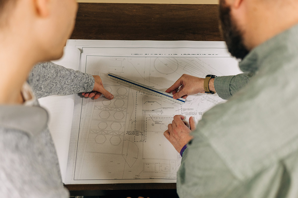 two men looking at plans, one with ruler in hand